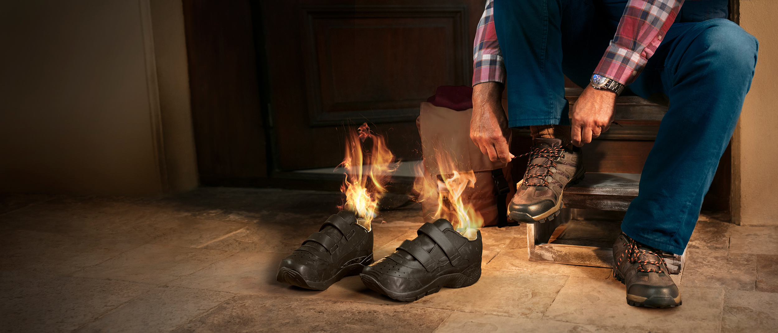 Illustration of a person on front steps of their house putting shoes on in preparation for a hike as the inside of shoes next to him are on fire