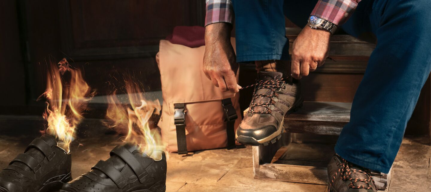 Illustration of a person on front steps of their house putting shoes on in preparation for a hike as the inside of shoes next to him are on fire